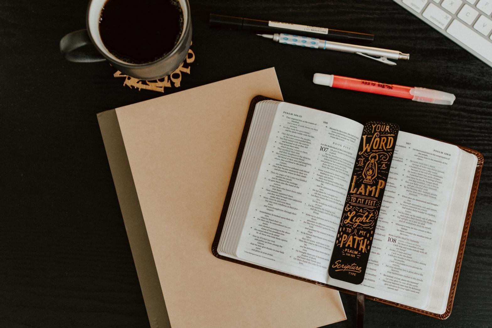 Open book on a desk with a bookmark, a cup of coffee, and pens