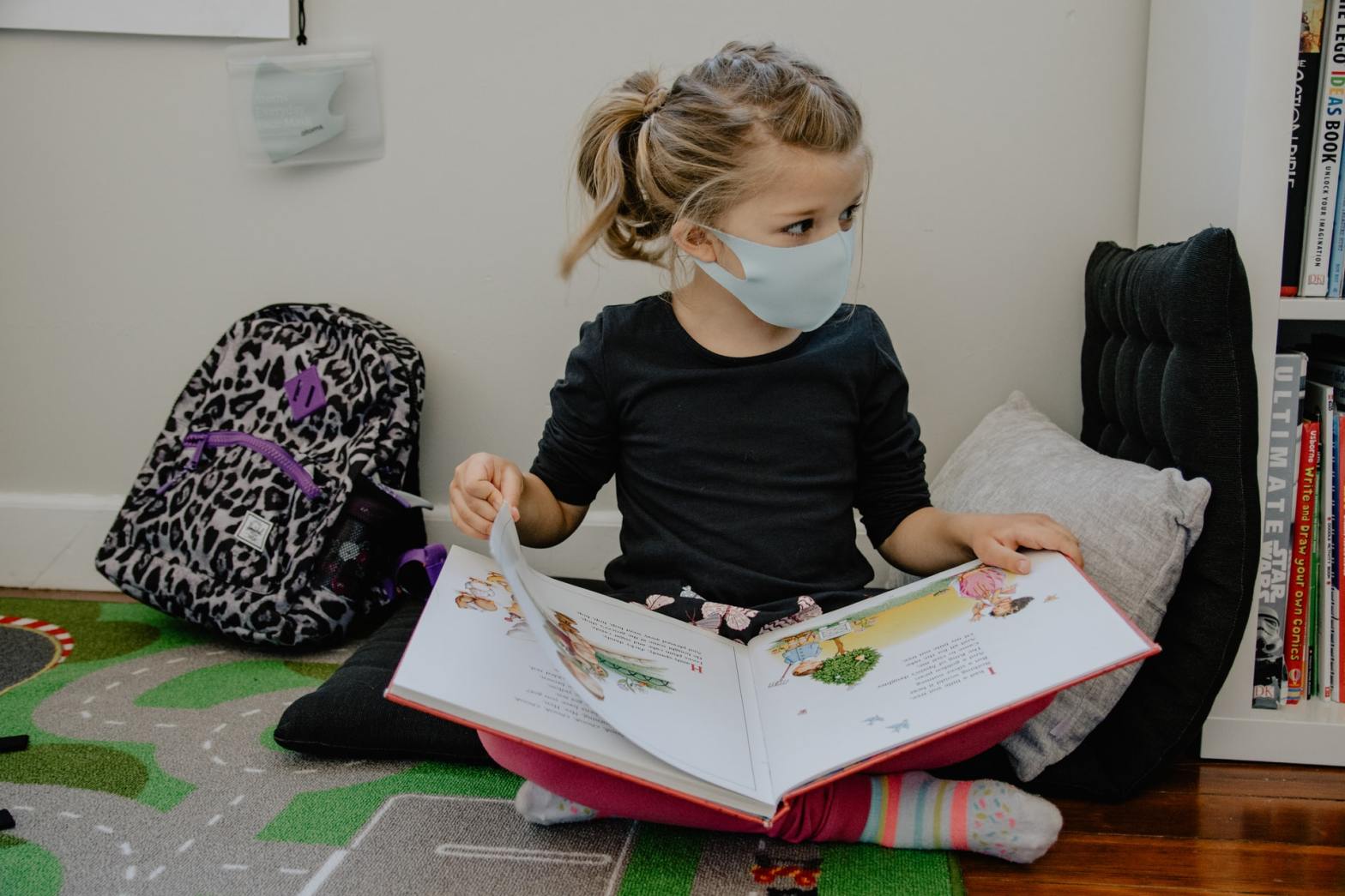 A little girl wearing a mask and holding an open book
