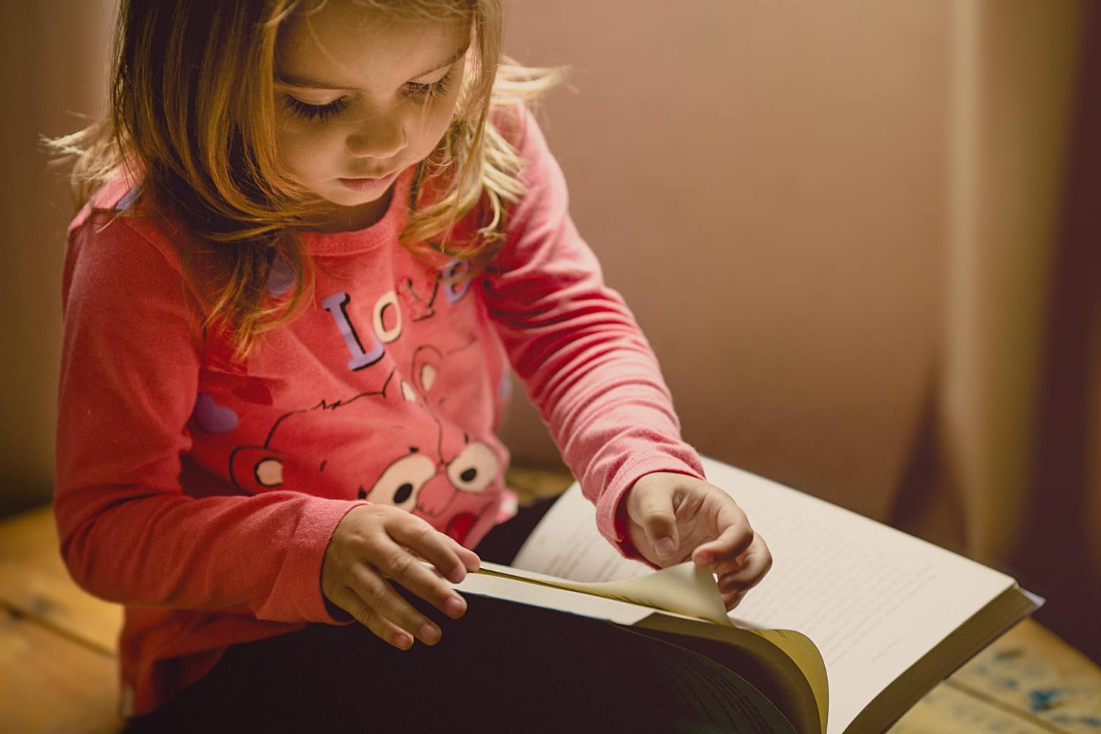 A little girl in pink reading a book