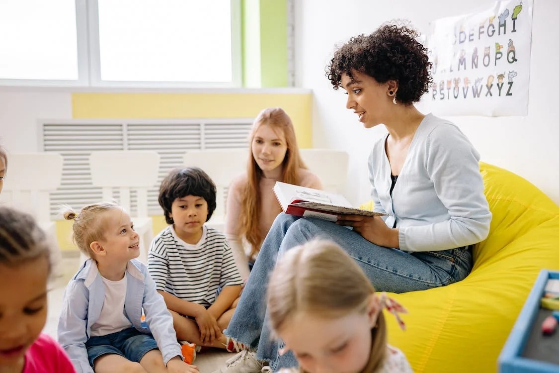 A woman reading a book in front of children.