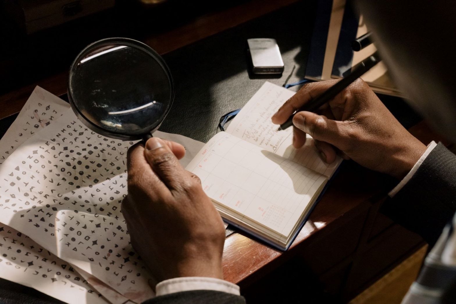 A man trying to decipher a code using a magnifying glass and his notes.