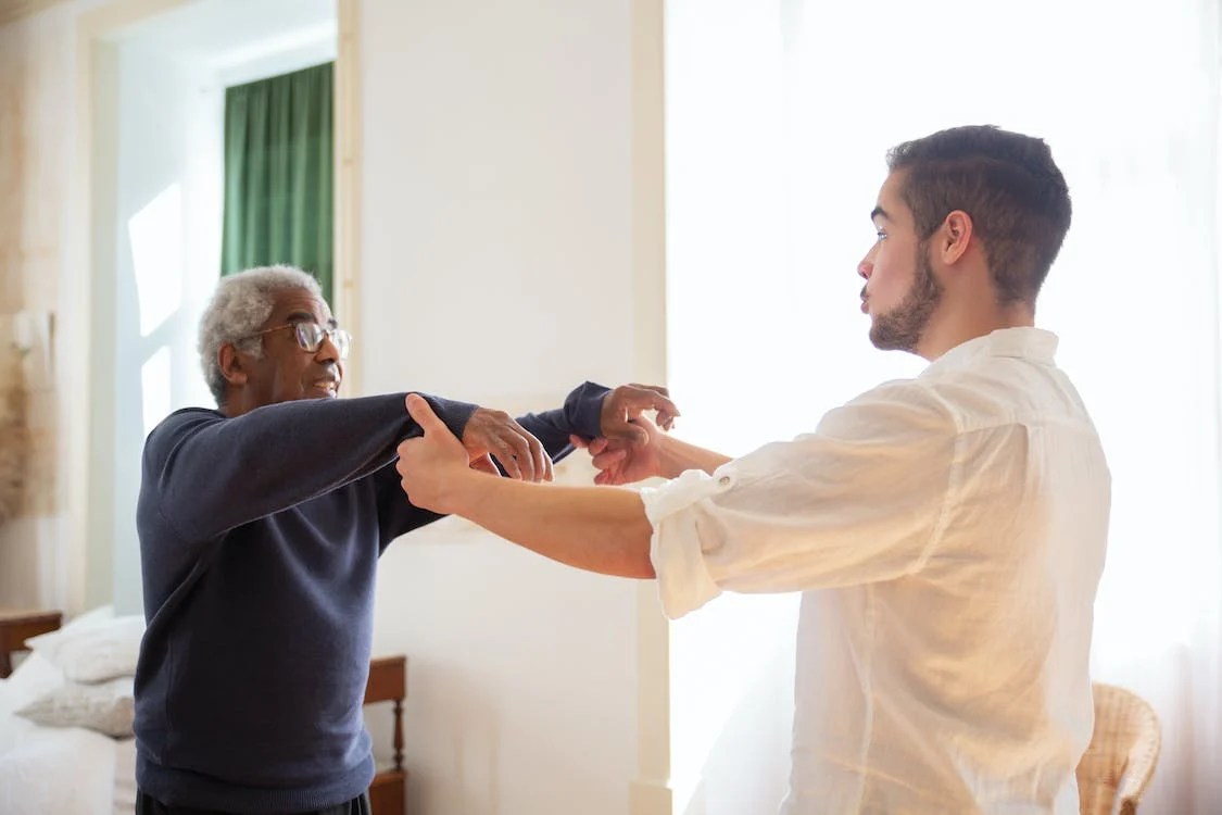 An elderly man talking to a young man while holding hands.