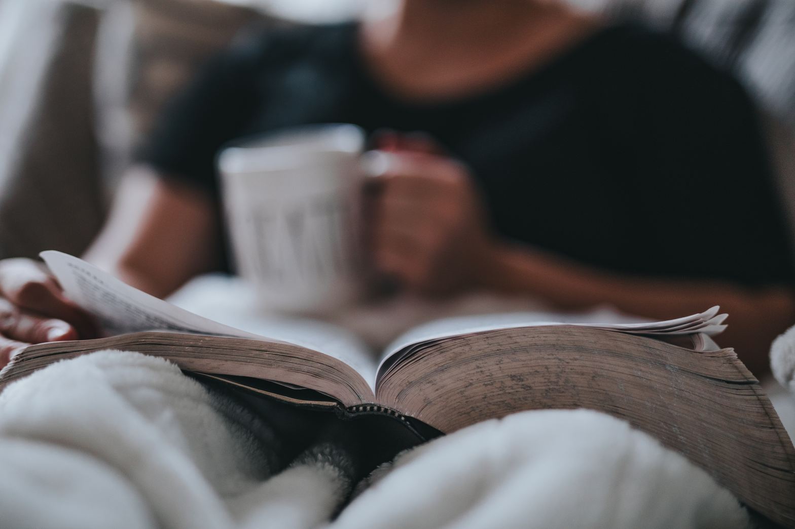 A person relaxing on their bed while reading a book.